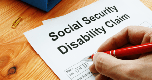 A person filling out a social security disability claim form with a pen and documents on a desk.