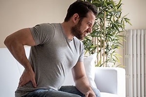 man-with-back-pain-from-injury-at-home-sitting-on-couch